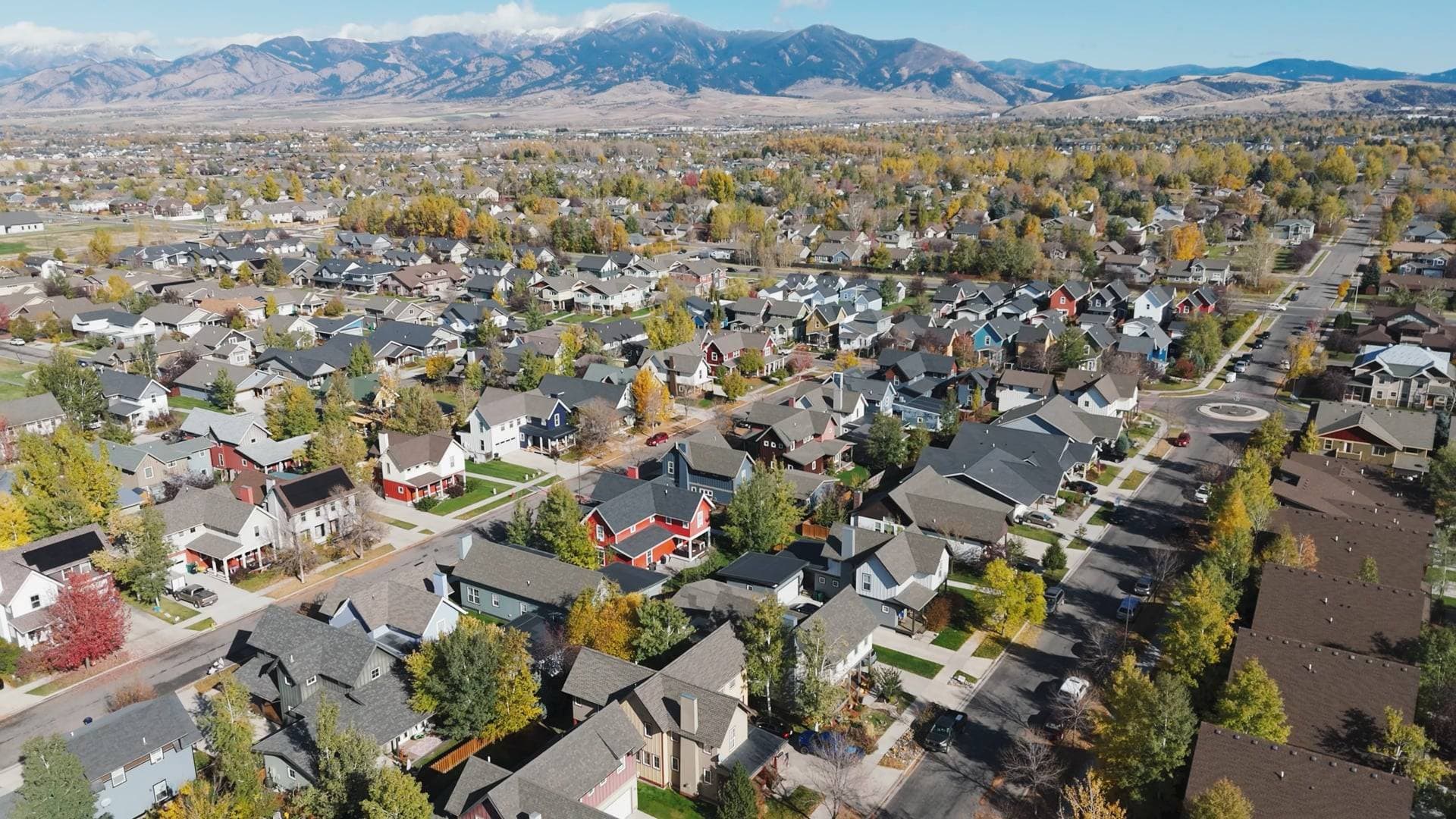 Aerial over a Bozeman subdivision of rooftops and autumn trees with the mountain range on the horizon
