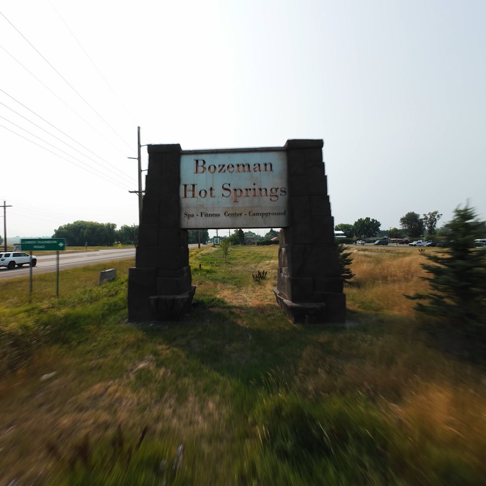 Stone entrance sign reading Bozeman Hot Springs standing in grass beside the highway