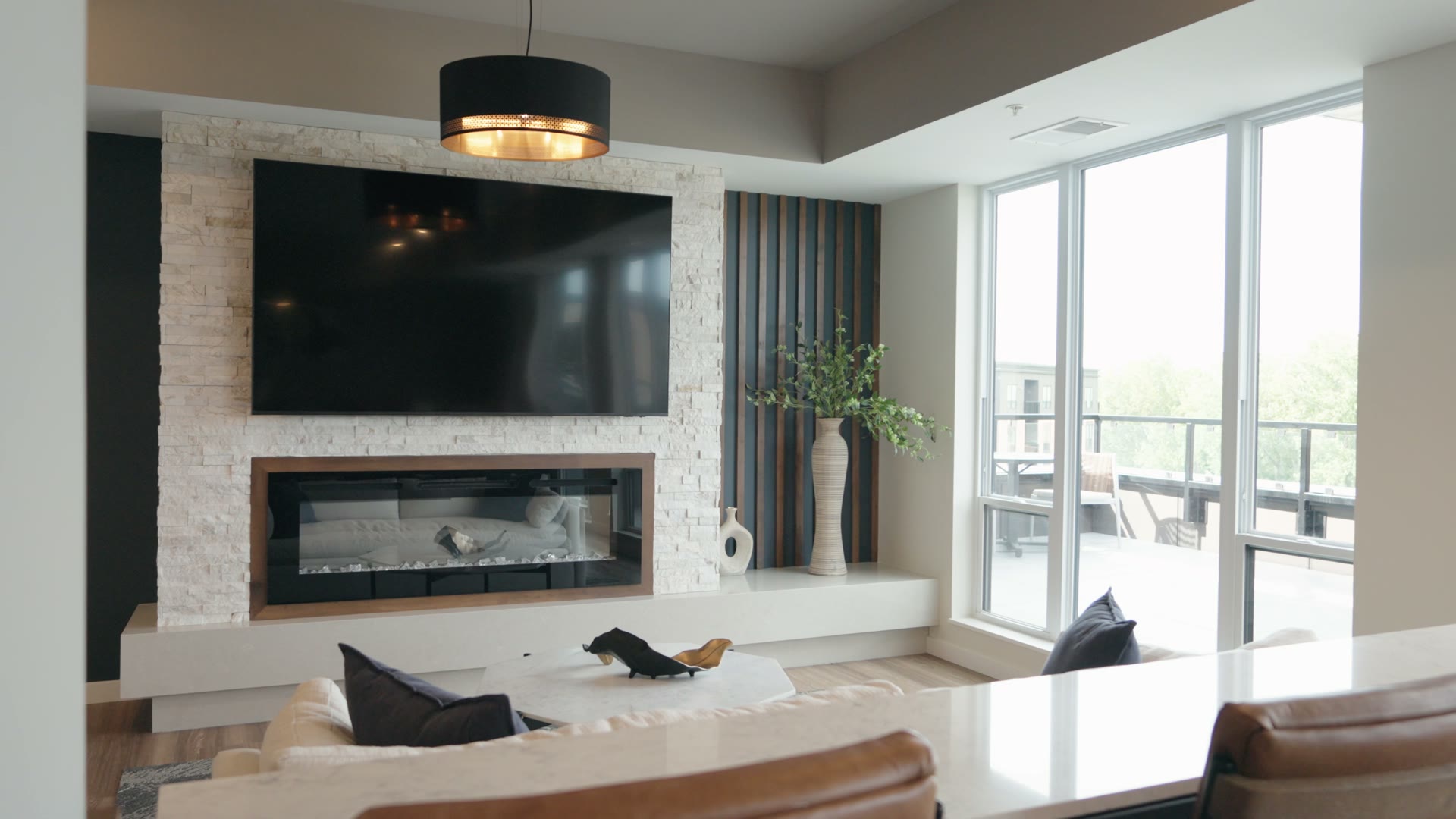 Living room at The Brooks with a mounted TV over a linear fireplace and a wall of balcony glass