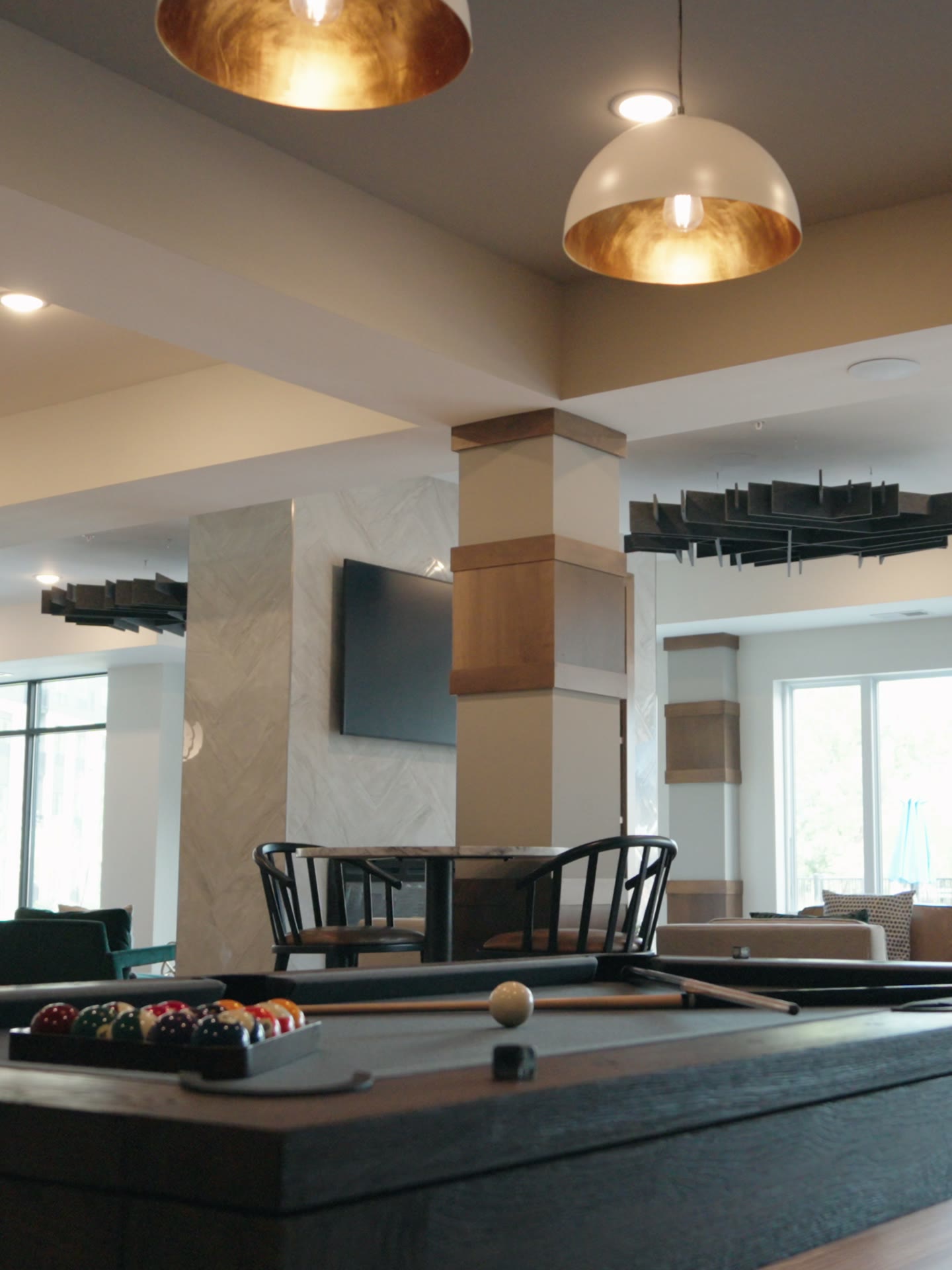 Clubroom at The Brooks with a shuffleboard table under brass dome pendants