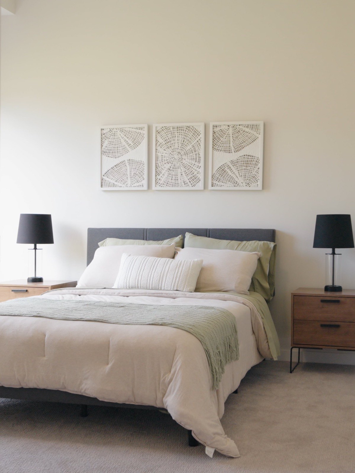 Staged bedroom at The Brooks with a made bed, matching lamps and three framed prints