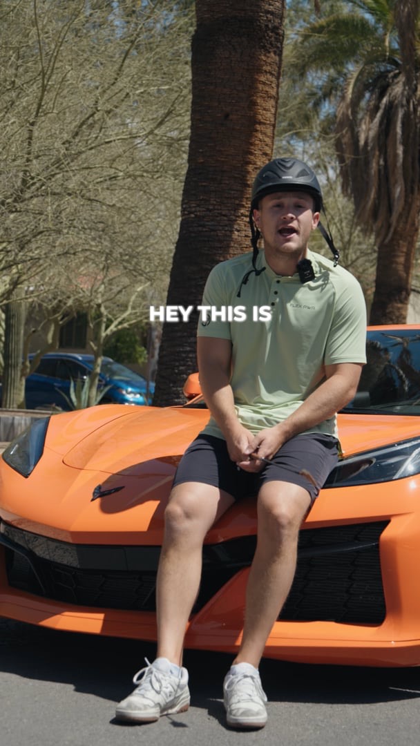 Flex PWR rep in a green polo sitting on the nose of an orange sports car, on-screen caption reading Hey this is